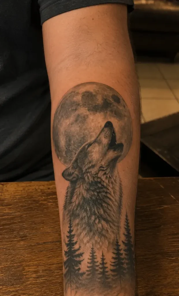 A howling wolf tattoo against a solid moon. The clean circle gives the eye an anchor, which is why the moon-and-howl pairing is one of the strongest forearm compositions.